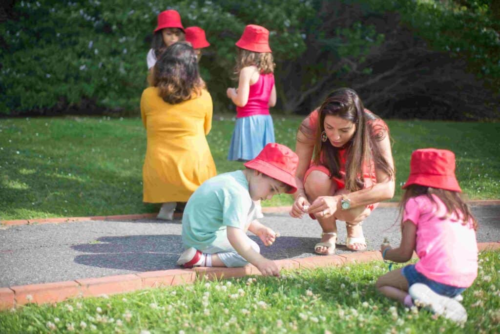 Practitioner helping preschool children explore nature outdoors during a summer activity.